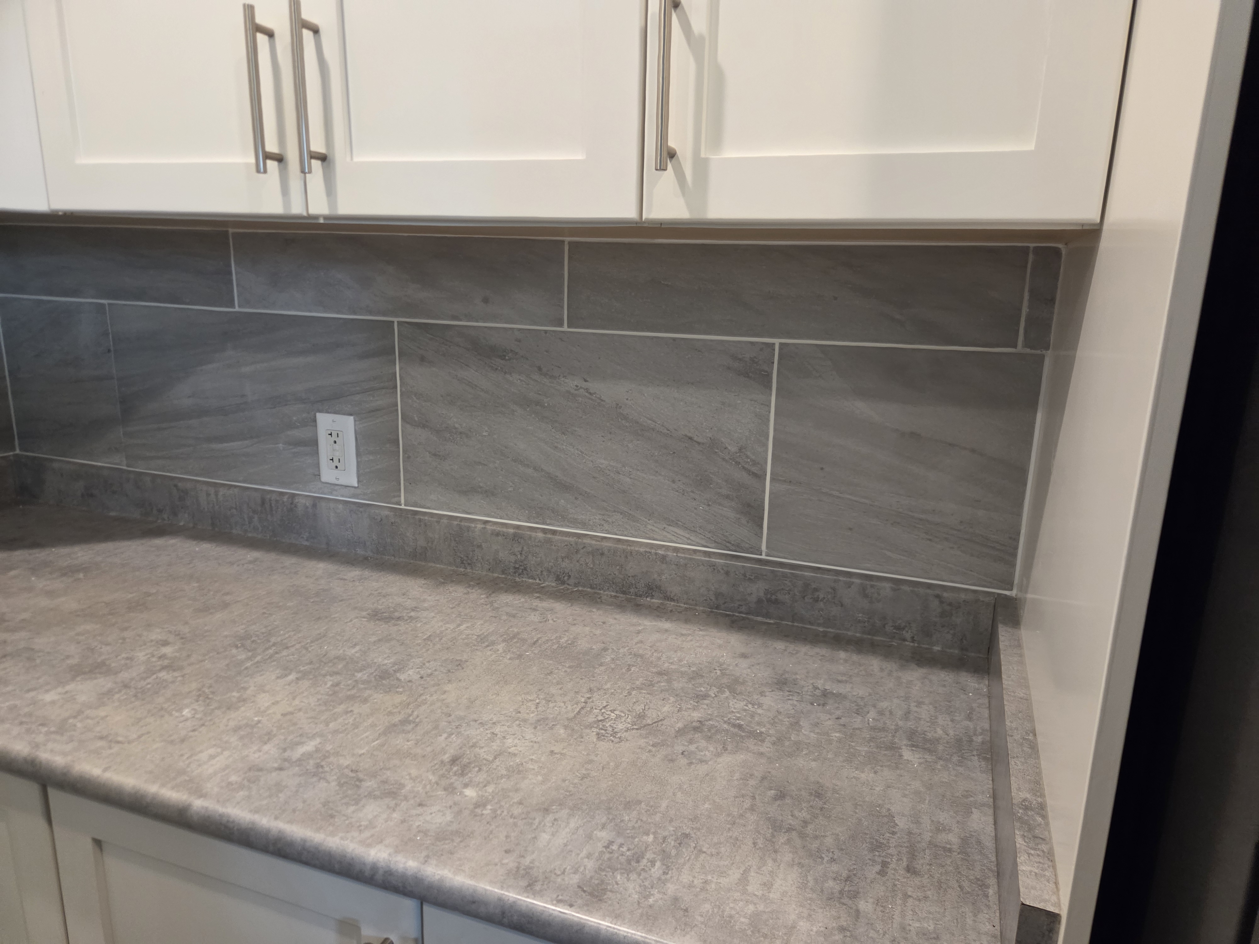 Finished kitchen with grey stone backsplash, white cabinets, and grey countertops